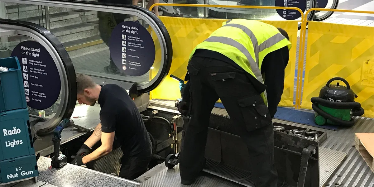 Two technicians repair an opened escalator at Liverpool Street station in London